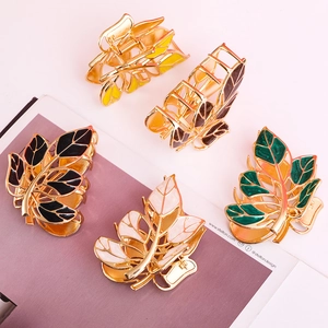 Close-up of five leaf-shaped metal hair claws in black, white, green, yellow, and brown