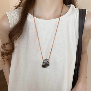 Detailed view of silver shell pendant with engraved textures on a brown woven cord