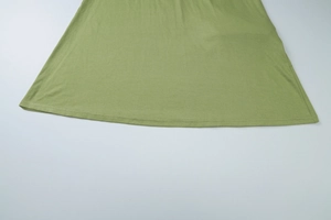 Detail of green fabric hem showing fine stitching and soft cotton texture on a long dress