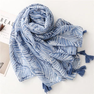 Detail of blue and white leaf pattern scarf with fringe tassels on a folded layout