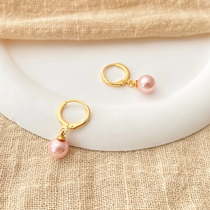 Detail of pink pearl drop earrings with 18K gold-plated hoops on beige linen texture