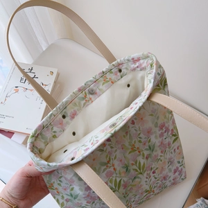 Close-up of floral tote bag showing faux leather straps and metal snap button closure
