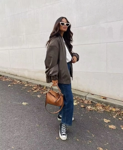Detail view of a brown bomber jacket styled with a knit top and straight-leg denim jeans