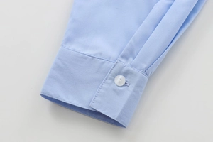 Close-up of light blue cotton shirt cuff featuring a white button and fine stitching detail