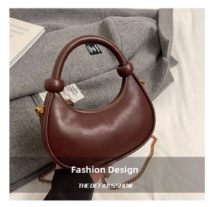 Detail view of a dark brown crescent moon bag with gold chain and beaded handle on cashmere