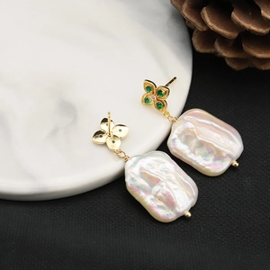 Baroque pearl earrings with golden clover studs and green gemstones on marble surface