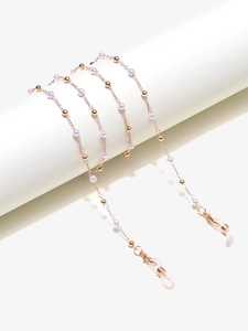 Detail of golden metal eyewear chain featuring purple pearls on a white display