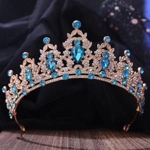 Close-up of golden crown with pear-cut blue crystal and intricate rhinestone leaves