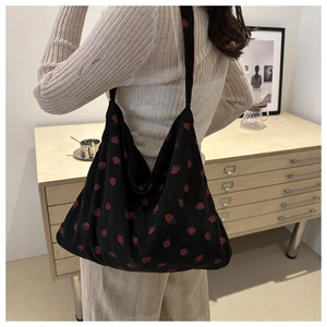 Black corduroy tote bag with red strawberry pattern shown in a cozy indoor setting