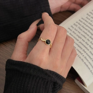 Minimalist gold wavy ring with black agate stone shown on model's finger with a book
