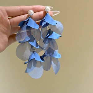 Détail de boucles d'oreilles à pétales bleus avec perle blanche et design à pampilles