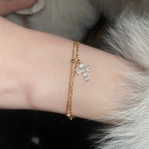 Detail of double-layer gold cross bracelet with sparkling zircon stones on female wrist