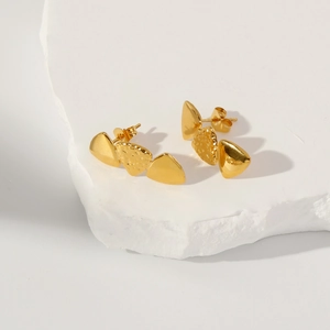 Detail of gold geometric earrings with lava texture on white stone pedestal
