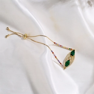 Detail of adjustable gold bracelet featuring a green marquise stone eye on white silk fabric