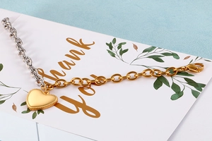 Detail of two-tone gold and silver link chain bracelet with a matte heart pendant on a card