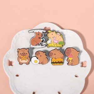 Set of six cute capybara enamel pins in various poses on a white decorative plate