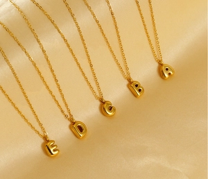 Detail view of five 3D golden bubble initial necklaces on champagne silk background