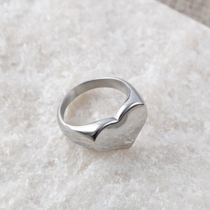 Close-up of polished silver heart ring in stainless steel on a white textured surface