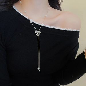 Detail of 18k gold plated long necklace with bow design and tassel pearls on a model