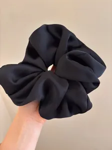 Macro detail of oversized black satin scrunchie showing uniform pleats and fabric texture