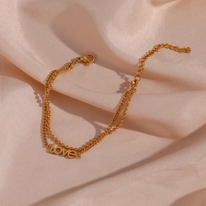 Macro detail of a double-layer gold chain bracelet with LOVE pendant on pink silk
