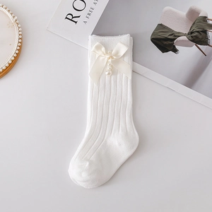 Detail of white cotton baby socks featuring cream bows, pearls and vertical knit texture