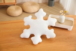 Detailed close-up of a white plush snowflake-shaped cushion on a wooden table surface