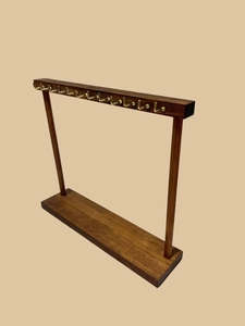 Detail of dark wood necklace display stand with multiple golden metal hooks on top bar