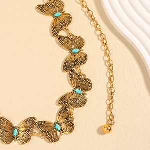Detailed shot of golden butterfly chain belt featuring turquoise stone inlays on textured surface