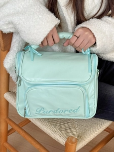 Close-up of mint green ballet style cosmetic bag with handle and embroidered logo