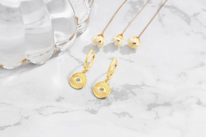 Macro detail of gold S925 silver Evil Eye earrings with sparkling zircon on marble