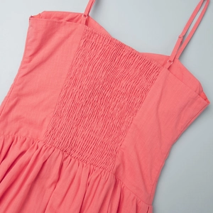 Detail of coral red smocked dress featuring adjustable spaghetti straps and cotton fabric