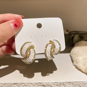 Detailansicht goldener gedrehter Ohrringe mit Muscheleinlage und glitzernden Steinen