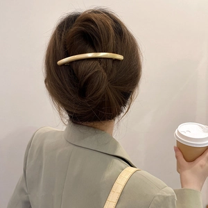 Elegant gold curved bar hair clip accessory worn on a sophisticated bun hairstyle
