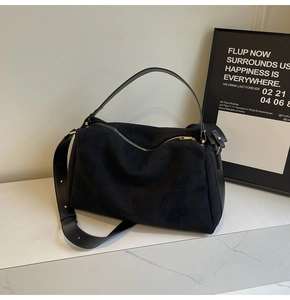 Close-up of black suede tote bag with leather strap and gold hardware on marble