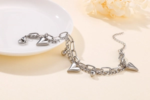 Detailed close-up of a silver double-layer heart charm bracelet on a warm beige background