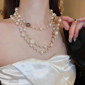 Detail of elegant three-layer pearl necklace with gold chain and daisy pendants