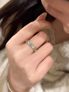 Detail of 18k gold plated flower ring with blue enamel, red gems and pearls on finger
