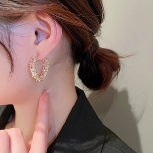 Close-up of a gold geometric C-shaped earring with clear rectangular zircons on model