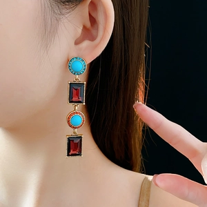 Close-up of vintage gold earrings with turquoise and deep red gemstone accents on a model