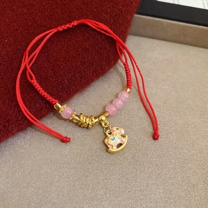 Dettaglio del bracciale in corda rossa intrecciata con cavallo a dondolo oro e perla rosa
