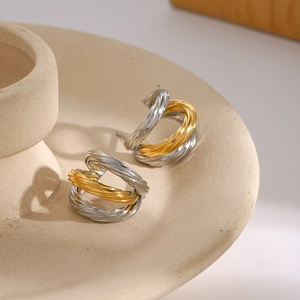 Macro shot of twisted two-tone gold and silver C-shaped metal earrings on ceramic