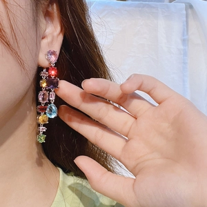 Macro detail of colorful faceted gemstone earrings featuring vibrant teardrop and square crystals