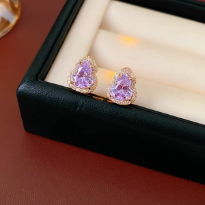 Macro detail of gold-tone gourd earrings with purple stones and sparkling zircons