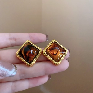 Close-up of square gold-rimmed earrings with amber marble texture worn on a finger