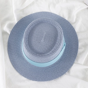 Top view of blue straw hat with light blue silk band on white textured background