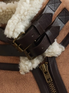 Detail of faux shearling collar and brown suede fabric with metallic buckles and zipper
