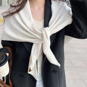 Gros plan d'un châle en tricot crème sur manteau noir montrant la texture et le style de superposition