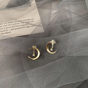 Détail des boucles d'oreilles lune et étoile dorées avec zircons sur tulle sombre
