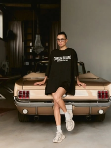 Oversized μαύρο βαμβακερό T-shirt με λευκό τύπωμα φορεμένο από μοντέλο δίπλα σε αυτοκίνητο